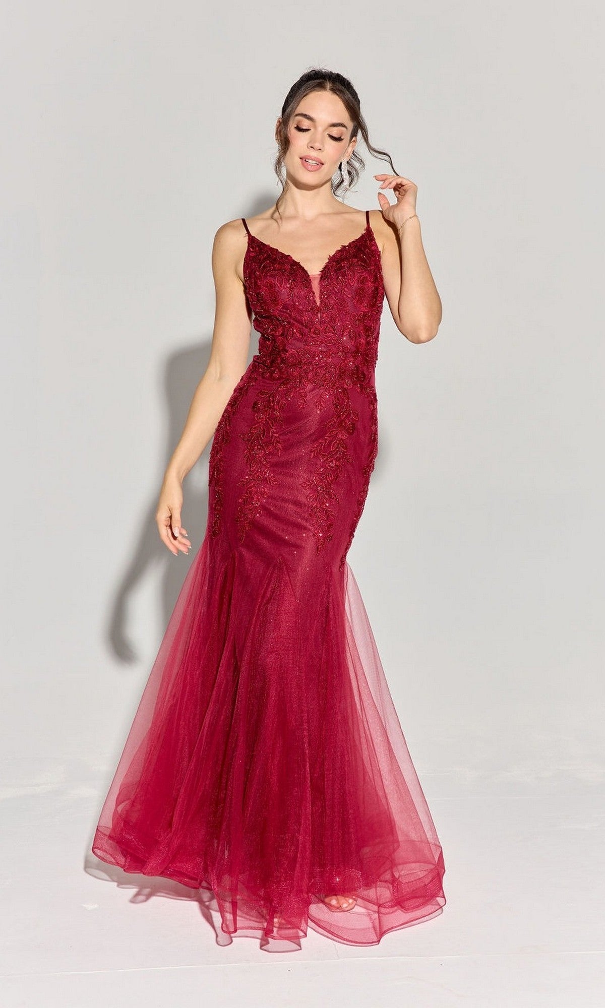 A woman wearing the Eureka 9998 long prom dress in burgundy, featuring a fitted, sleeveless silhouette with a beaded floral design and tulle detailing, stands against a plain light background.